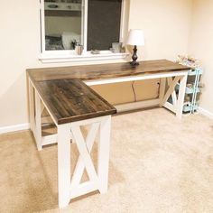 a wooden desk sitting in the middle of a living room next to a white window