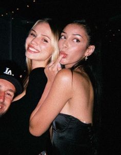 two beautiful young women standing next to a man in a black dress at a party