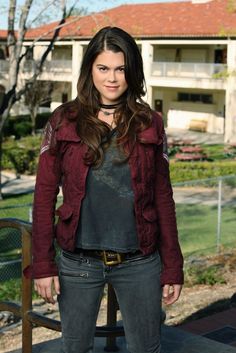 a woman standing in front of a building wearing a red jacket and black shirt with her hands on her hips