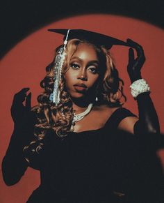 a woman in a graduation cap and gown holding her hand up to her head while standing against a red background