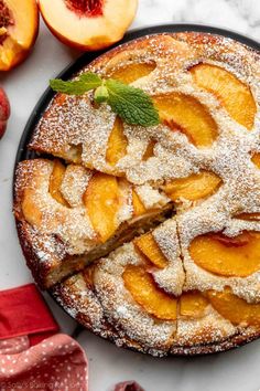 a pie with slices cut out and topped with powdered sugar next to sliced peaches