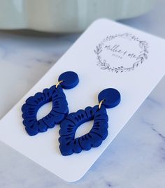 a pair of blue earrings sitting on top of a white plate next to a plant