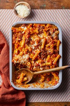 a casserole dish filled with pasta and meat on a striped cloth next to a wooden spoon