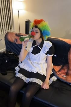 a woman sitting on a couch with a clown wig drinking from a green beer bottle