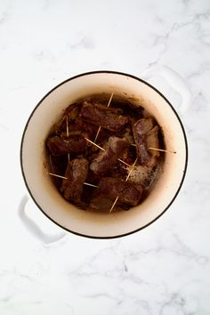 a pot filled with meat and toothpicks on top of a white countertop