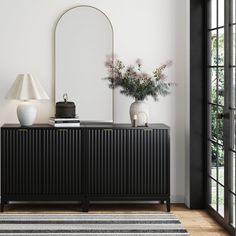 a white vase with flowers on top of a black cabinet in front of a mirror