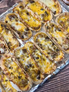 some tacos sitting on top of tin foil covered in cheese and other toppings