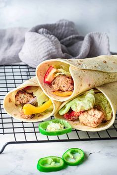 three pita wraps with meat and vegetables on a cooling rack next to green peppers