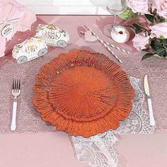 an orange plate sitting on top of a table next to silverware and pink flowers