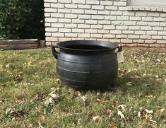 a large black pot sitting on top of a grass covered field next to a brick building