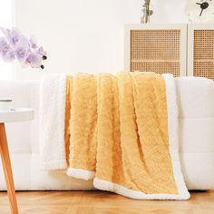 a white couch with a yellow blanket on top of it next to a wooden table