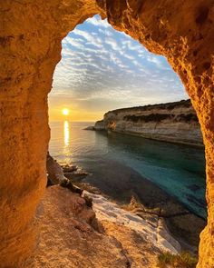 the sun is setting over the ocean through an arch in a rock formation with water below