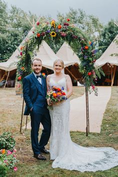 a bride and groom standing in front of a floral arch at their outdoor wedding ceremony