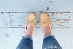 a person wearing yellow shoes standing on top of a white wooden floor with ripped jeans