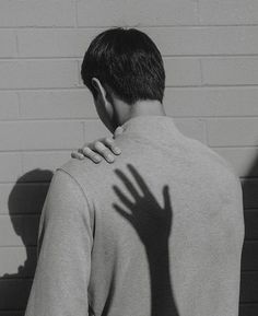 the shadow of a person's hand on their back as they stand in front of a brick wall