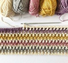 crochet yarn and knitting needles laid out on top of a white surface with multicolored skeins