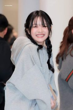 a woman with long black hair wearing a gray hoodie and smiling at the camera