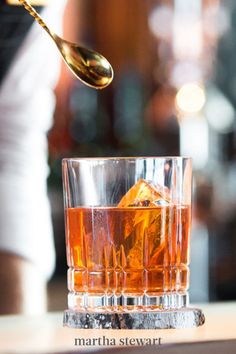 a woman is spooning ice into a glass with an orange peel in the middle