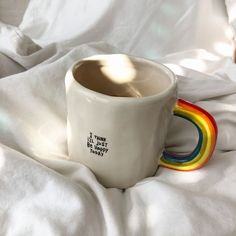 there is a coffee cup with a rainbow handle on the white bed sheet and it says, that's not all happy today