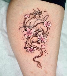 a woman's thigh with a dragon and flowers tattoo design on the side of her leg