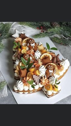 a cake is decorated with various types of food on top of paper and surrounded by pine branches