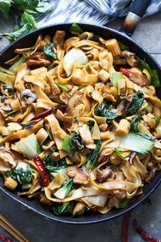 a skillet filled with noodles and vegetables on top of a table next to chopsticks