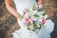 a bride holding a bouquet of pink and white flowers on her wedding day in the woods