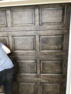 a man in grey shirt and black pants painting a wooden garage door