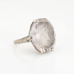 Finely detailed vintage Art Deco rock crystal intaglio ring (circa 1920s to 1930s) crafted in 18 karat white gold.   Oval cut rock crystal measures 18mm x 15mm. The rock crystal is in good condition with light wear evident under a 10x loupe.  The striking Art Deco era ring features an intaglio depicting the bust of a Roman soldier. The lacy filigree mount is a hallmark of Art Deco era jewelry with crisp details including a foliate pattern and an intricate openwork design. The ring has a medium profile and rises 7.5mm from the finger (0.29 inches).    The ring is in good condition and was lightly cleaned and polished.   Particulars:  Weight: 5.1 grams  Stones:  Oval cut rock crystal measures amethyst measures 18mm x 15mm. The rock crystal is in good condition with light wear evident under a Antique Silver Intaglio Ring, Intaglio White Gold Ring, Formal Carved White Gold Engraved Ring, Carved White Gold Engraved Ring For Formal Occasions, Heirloom Silver Signet Ring With Intaglio, Silver Intaglio Signet Ring For Wedding, Silver Wedding Signet Ring With Intaglio, Formal Engraved White Gold Ring, Vintage Silver Ring With Intaglio