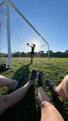 two people are sitting on the grass near a soccer goal and one person is kicking a ball