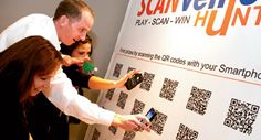 two women and a man are taking pictures with their cell phones as they stand in front of a qr - code wall