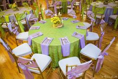 a green table topped with lots of purple and white chairs next to a vase filled with flowers