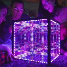 three people are looking at a computer screen that is lit up with colorful lights in the dark