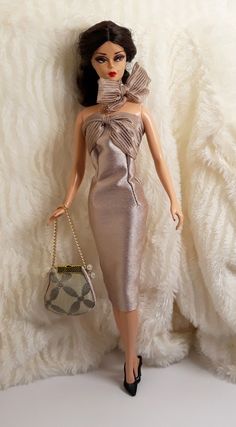 a barbie doll wearing a silver dress and holding a purse in front of a white background