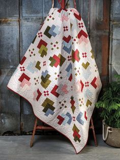 a quilted blanket sitting on top of a chair next to a potted plant