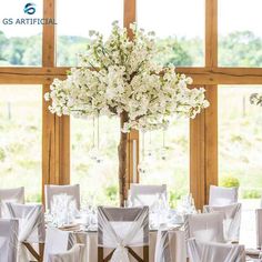 a tall vase with white flowers on top of a table in front of large windows