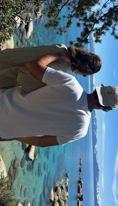 a man standing on the edge of a cliff looking out at the water and rocks