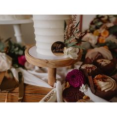 a white wedding cake sitting on top of a wooden stand next to other desserts