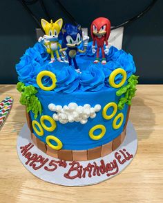 a birthday cake with sonic the hedgehog figures on top and blue frosting, sitting on a wooden table