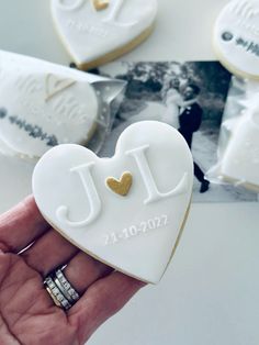 a hand holding a heart shaped cookie with the initials j and i on it, surrounded by other cookies