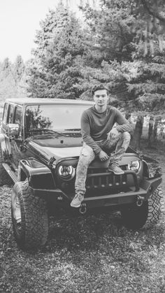 a man sitting on the back of a pickup truck in front of a wooded area