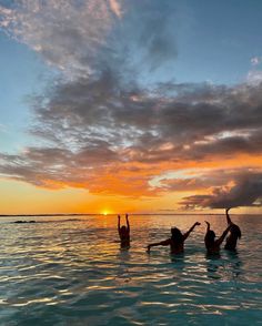 three people in the water at sunset with their arms up and one person raising his hand