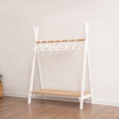 a white coat rack sitting on top of a wooden floor next to a potted plant