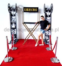 a man standing in front of a director chair on a red carpeted area with metal barriers