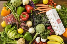 many different types of fruits and vegetables on a wooden table with one carton of eggs