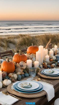 a table set with plates, candles and pumpkins on the sand near the beach