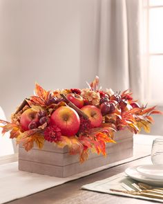 an arrangement of apples, grapes and leaves in a wooden box on a dining room table