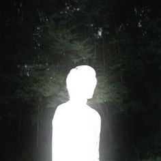 a person standing in the middle of a forest at night with their head turned to the side