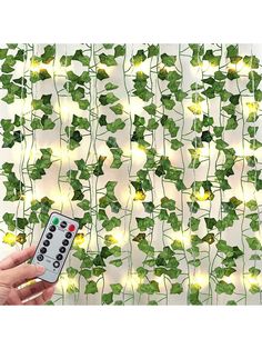 a hand holding a remote control in front of a wall with ivy vines on it