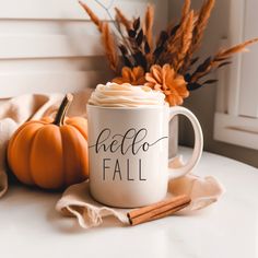 a white coffee mug with the words hello fall on it next to some pumpkins